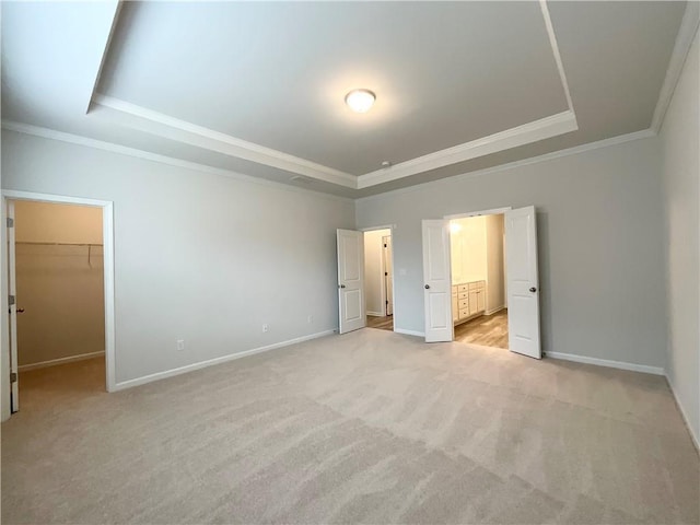 unfurnished bedroom with a walk in closet, ornamental molding, a tray ceiling, and light carpet