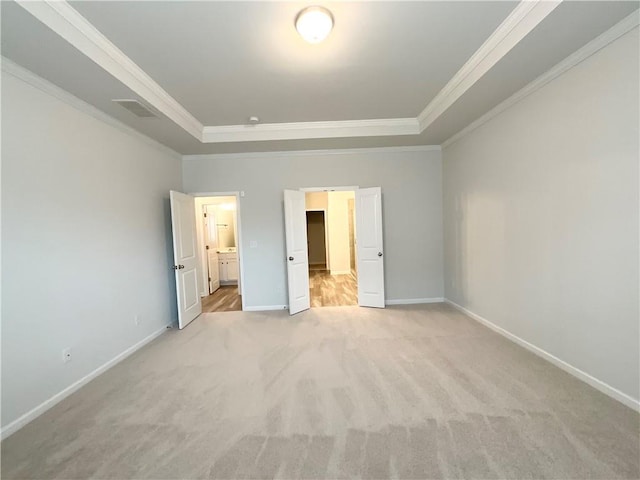 unfurnished bedroom featuring connected bathroom, a walk in closet, a tray ceiling, crown molding, and light carpet