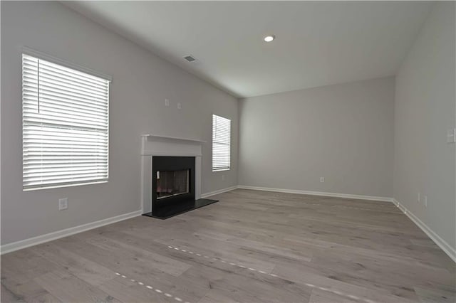 unfurnished living room with light wood-type flooring, a wealth of natural light, and lofted ceiling