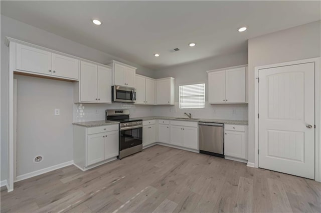 kitchen with sink, white cabinets, light hardwood / wood-style floors, and appliances with stainless steel finishes