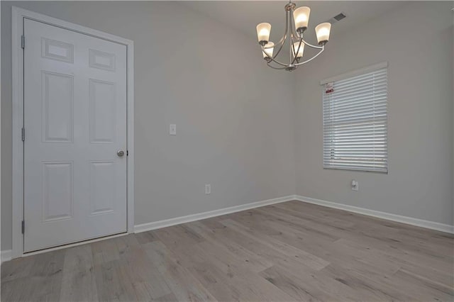 spare room featuring a notable chandelier and light wood-type flooring