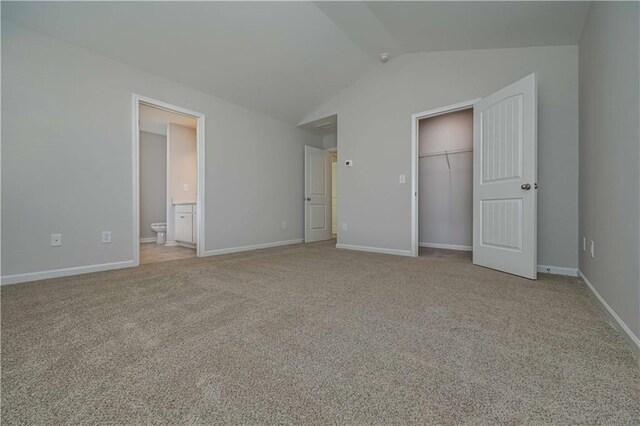 unfurnished bedroom with light carpet, a walk in closet, connected bathroom, a closet, and lofted ceiling