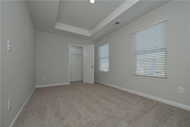 unfurnished bedroom with a raised ceiling, a closet, and light colored carpet