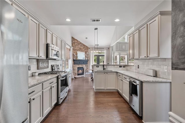 217 Springs Xing, Canton, GA 30114 - kitchen featuring appliances with stainless steel finishes, a fireplace, dark wood-style floors, decorative backsplash, and a peninsula