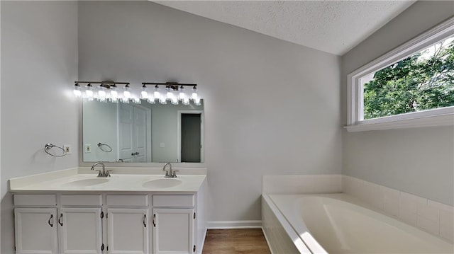 bathroom featuring a garden tub, double vanity, a textured ceiling, wood finished floors, and baseboards
