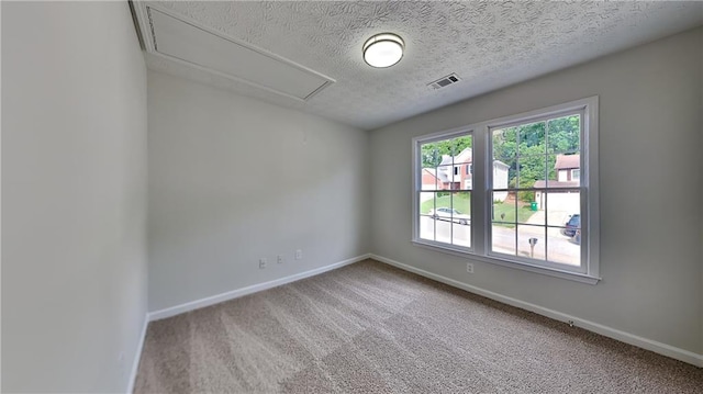 carpeted spare room with attic access, baseboards, and a textured ceiling