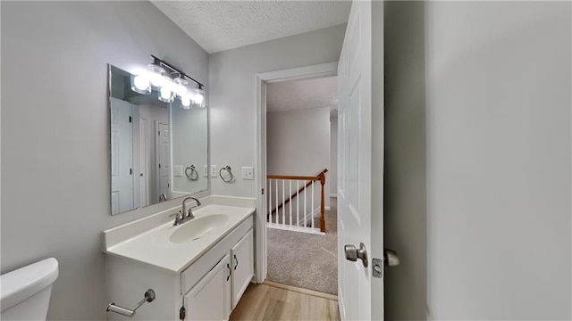 half bath with toilet, a textured ceiling, vanity, and wood finished floors