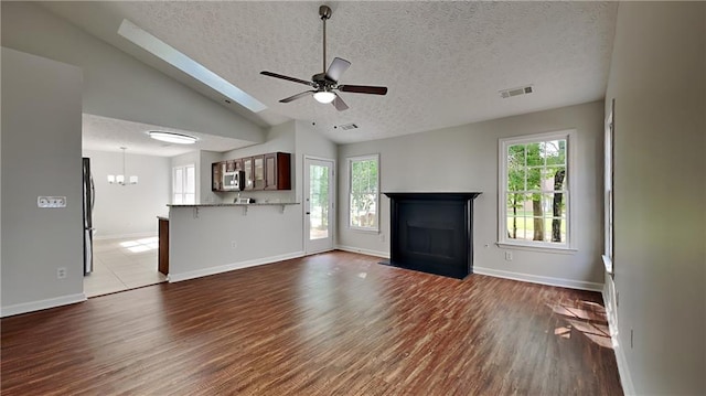 unfurnished living room featuring a textured ceiling, wood finished floors, a fireplace with flush hearth, baseboards, and ceiling fan