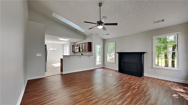 unfurnished living room with wood finished floors, plenty of natural light, a fireplace, a textured ceiling, and a ceiling fan