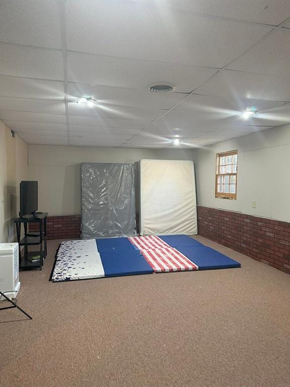 interior space with carpet, a paneled ceiling, and brick wall