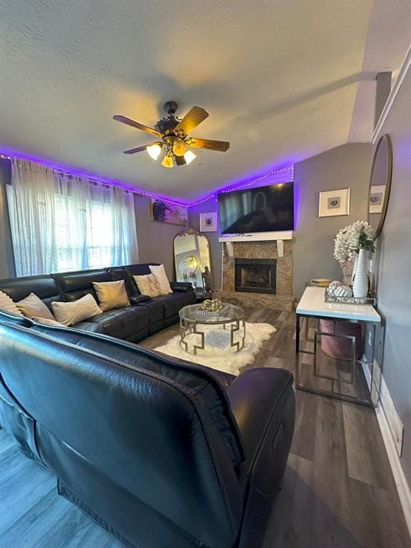 living room featuring hardwood / wood-style floors, ceiling fan, a stone fireplace, and lofted ceiling