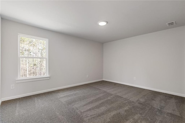 empty room with dark carpet, visible vents, and baseboards