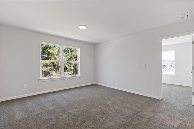 empty room featuring dark carpet, plenty of natural light, visible vents, and baseboards
