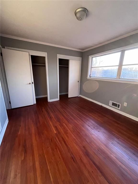 unfurnished bedroom with two closets, dark wood-type flooring, and ornamental molding