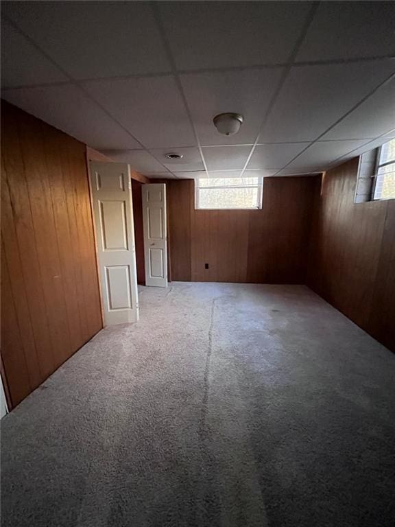 basement featuring a drop ceiling, carpet, and wood walls
