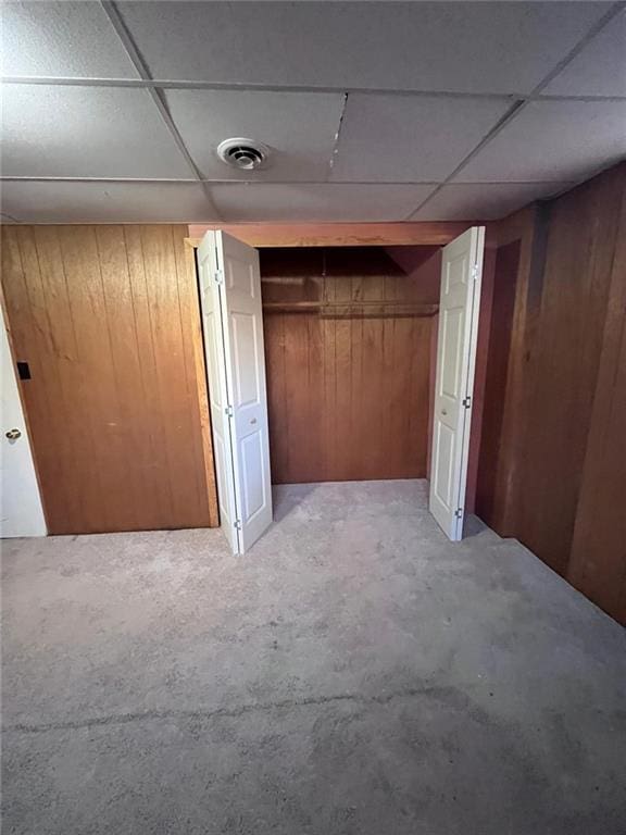 basement with a drop ceiling and wooden walls