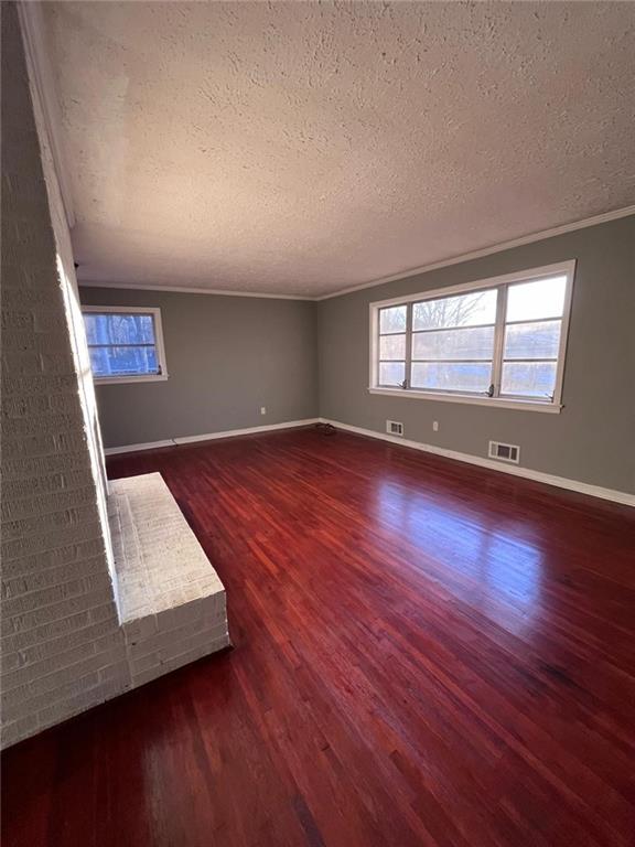 empty room with dark wood-type flooring, plenty of natural light, crown molding, and a textured ceiling