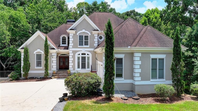 traditional-style home featuring a shingled roof, french doors, and stucco siding