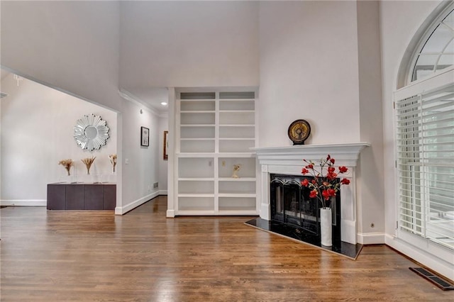 living area featuring a high ceiling, a fireplace, wood finished floors, visible vents, and baseboards