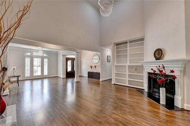 living area with a premium fireplace, wood finished floors, baseboards, decorative columns, and crown molding