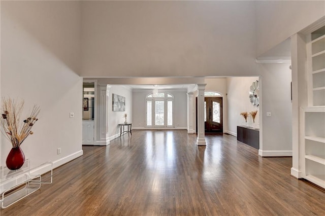 unfurnished living room with built in features, wood finished floors, decorative columns, and baseboards