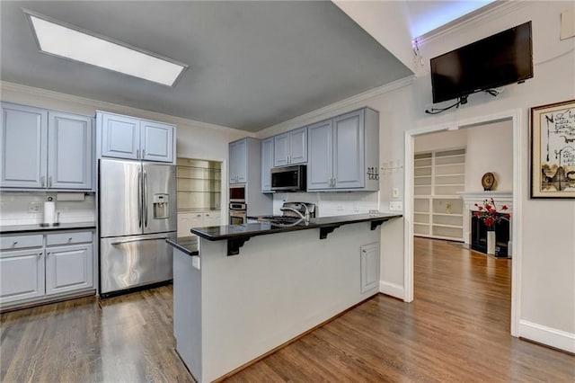 kitchen featuring dark wood finished floors, stainless steel appliances, dark countertops, a peninsula, and a kitchen bar