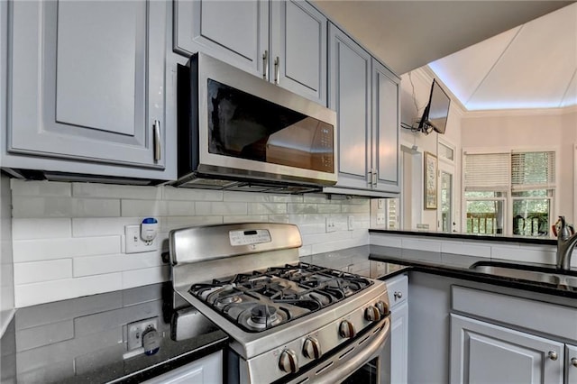 kitchen featuring stainless steel appliances, gray cabinets, a sink, and backsplash