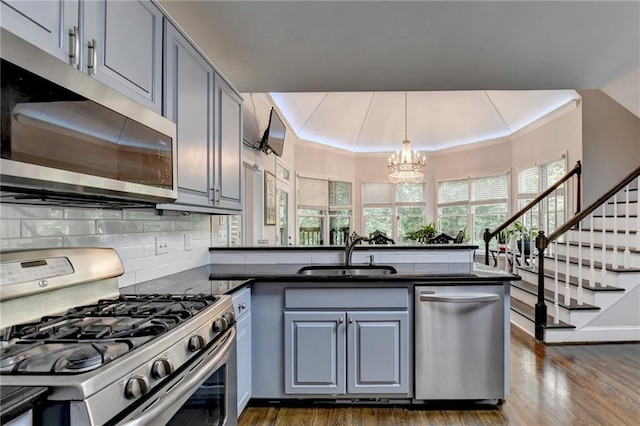 kitchen featuring stainless steel appliances, dark countertops, gray cabinetry, a sink, and a peninsula