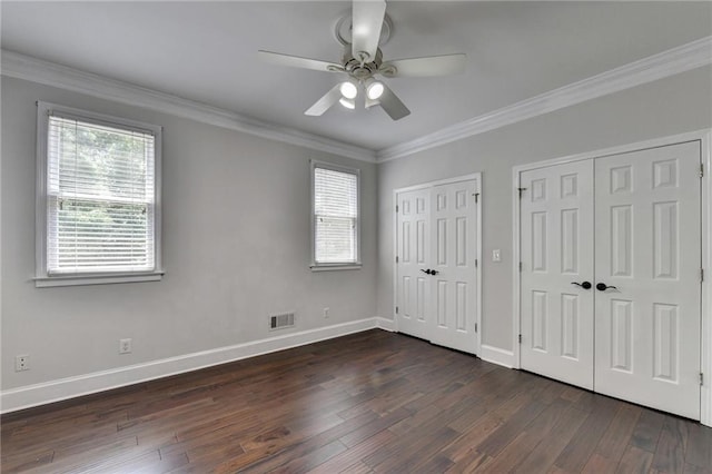 unfurnished bedroom featuring multiple closets, visible vents, ornamental molding, and dark wood-style floors