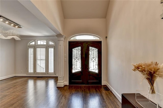 foyer entrance featuring dark wood-style floors, french doors, a notable chandelier, decorative columns, and baseboards