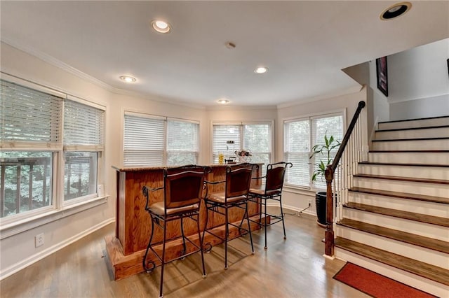 bar with a bar, light wood-style flooring, stairs, and crown molding