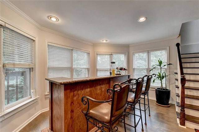 bar with dark wood-type flooring, baseboards, stairs, a bar, and crown molding