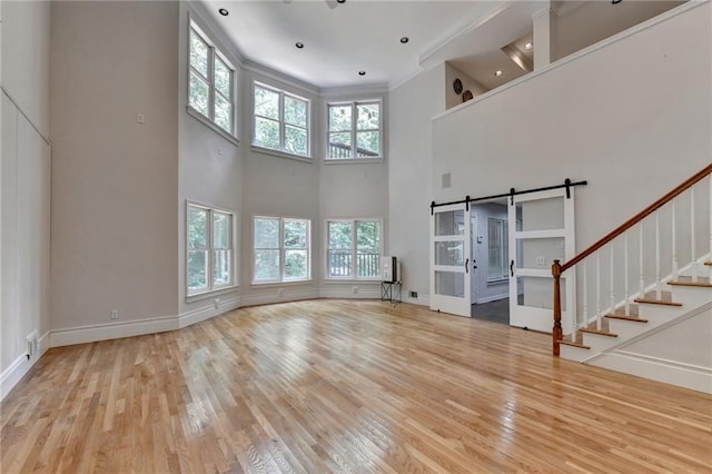 unfurnished living room with a barn door, stairway, wood finished floors, and a wealth of natural light