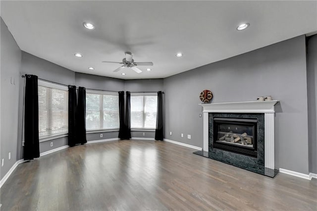 unfurnished living room with recessed lighting, wood finished floors, a high end fireplace, and baseboards