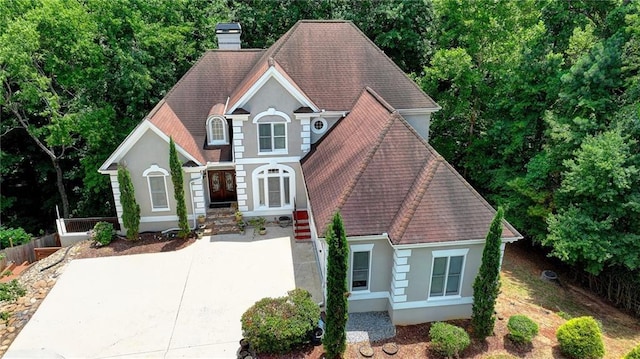 view of front of home with a shingled roof, concrete driveway, a chimney, and stucco siding