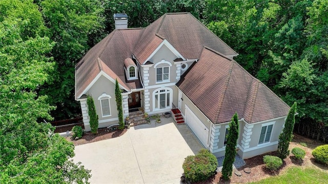 view of front of house with a shingled roof, concrete driveway, and a chimney