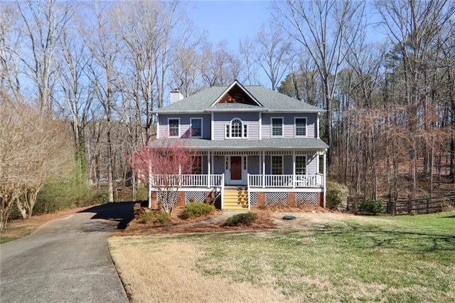 view of front of house with a chimney, covered porch, a front yard, a view of trees, and driveway