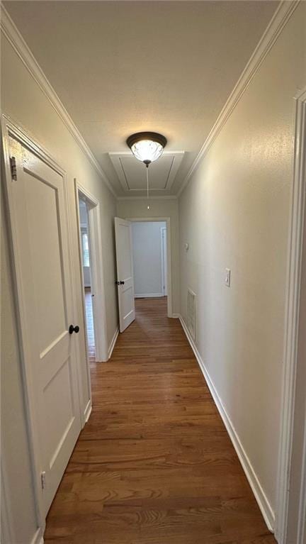 corridor featuring wood finished floors, attic access, baseboards, visible vents, and crown molding
