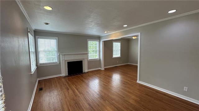 unfurnished living room featuring wood finished floors, a brick fireplace, baseboards, visible vents, and crown molding