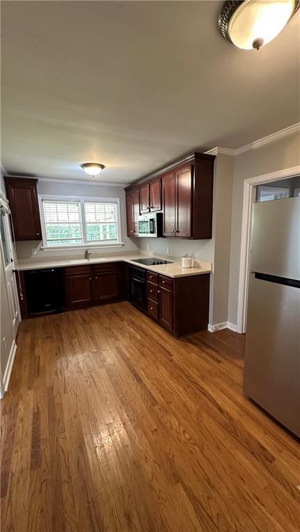 kitchen featuring wood finished floors, stainless steel appliances, light countertops, dark brown cabinets, and crown molding