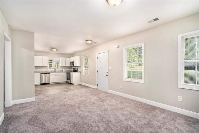 unfurnished living room with a wealth of natural light, sink, and light carpet