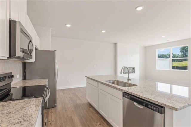 kitchen featuring a center island with sink, decorative backsplash, appliances with stainless steel finishes, white cabinets, and a sink