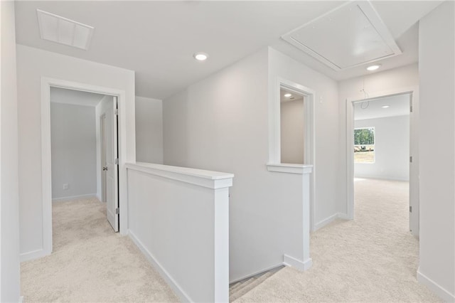 hallway with attic access, light carpet, visible vents, and an upstairs landing
