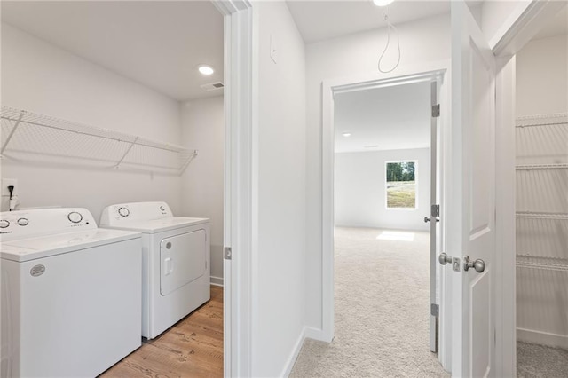 clothes washing area featuring washing machine and dryer, light carpet, laundry area, visible vents, and baseboards