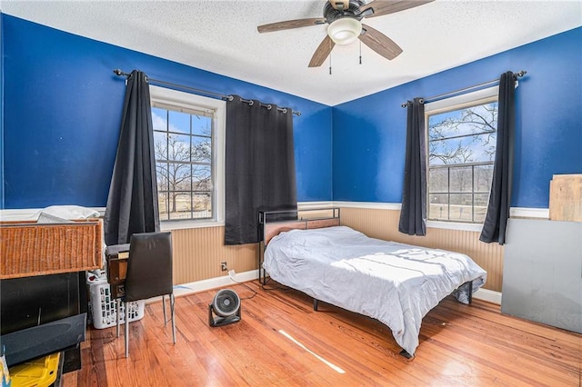 bedroom with a ceiling fan, a wainscoted wall, a textured ceiling, and wood finished floors