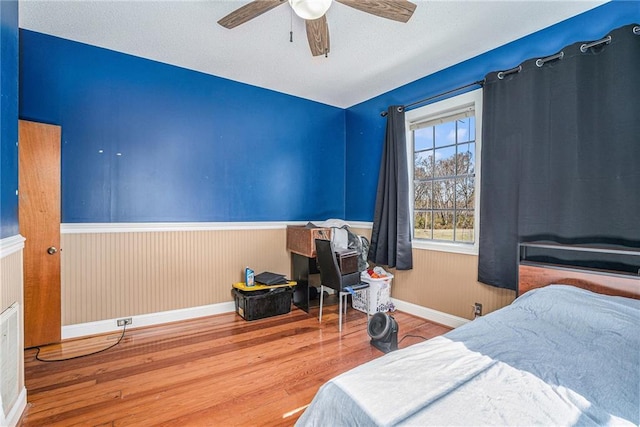 bedroom with a wainscoted wall, baseboards, a ceiling fan, and wood finished floors