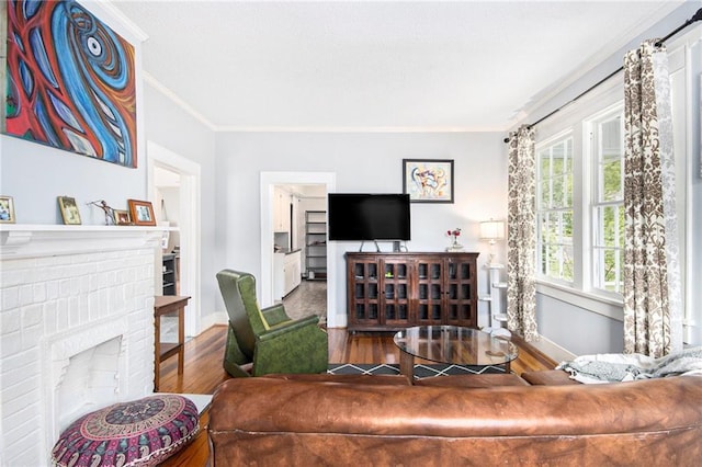 living room with a brick fireplace, wood finished floors, ornamental molding, baseboards, and a textured ceiling