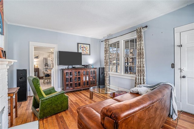 living area with baseboards, a brick fireplace, wood finished floors, and crown molding