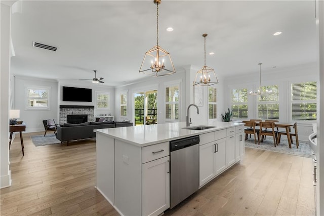 kitchen with light wood-type flooring, dishwasher, sink, a fireplace, and a center island with sink