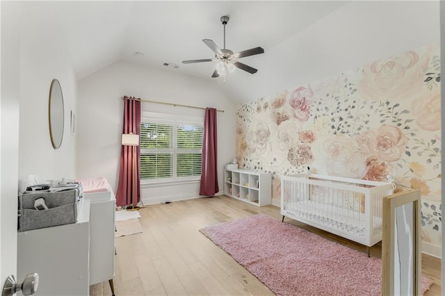 bedroom featuring a crib, light hardwood / wood-style flooring, ceiling fan, and lofted ceiling